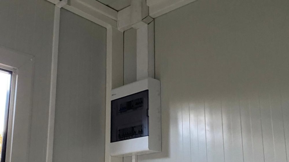 Surface-mounted consumer unit in a VeltHaven building, with the white trunking run following the ceiling junction and panel lines