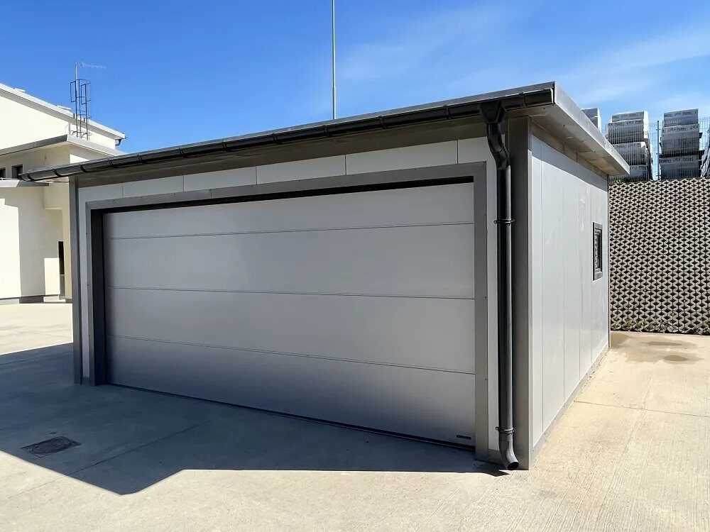 Light-grey insulated PIR garage with anthracite sectional door, front view on residential driveway