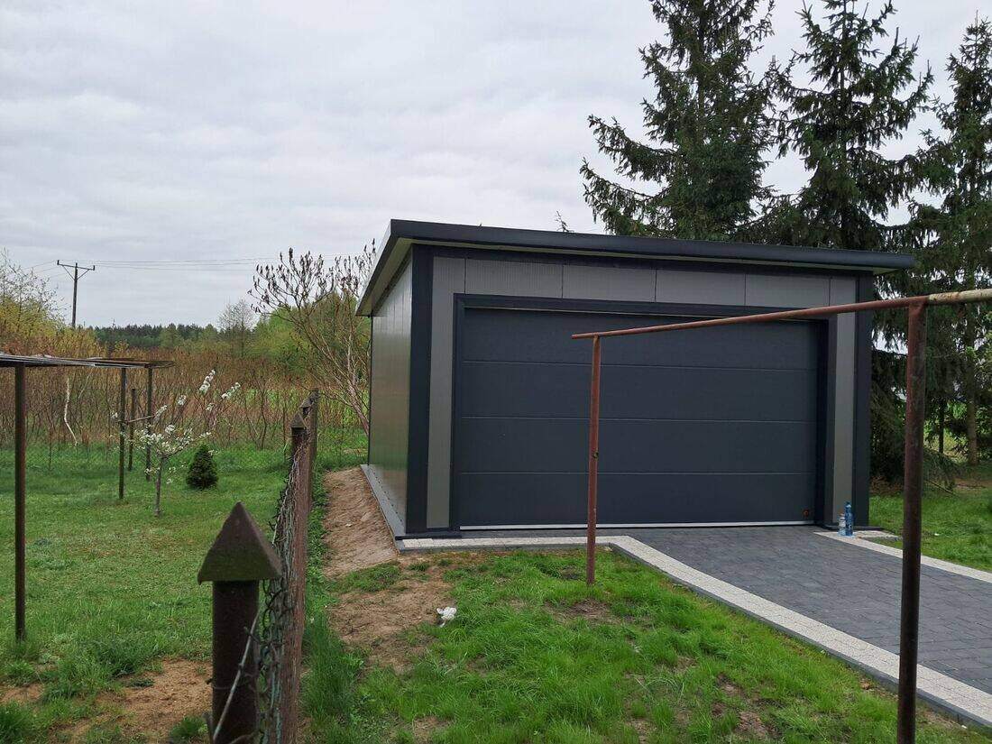 Anthracite insulated PIR garage, front-left view with tall conifer trees in background