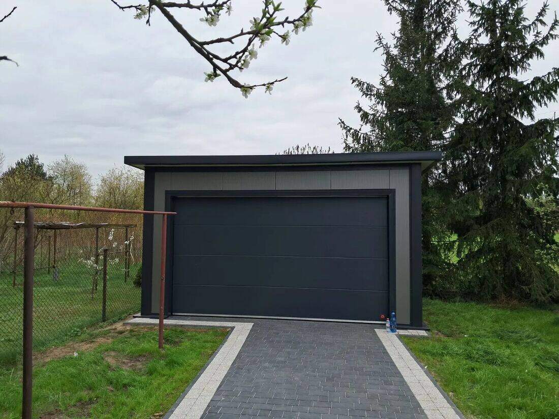 Anthracite insulated PIR garage, front-left three-quarter view with conifers in autumn