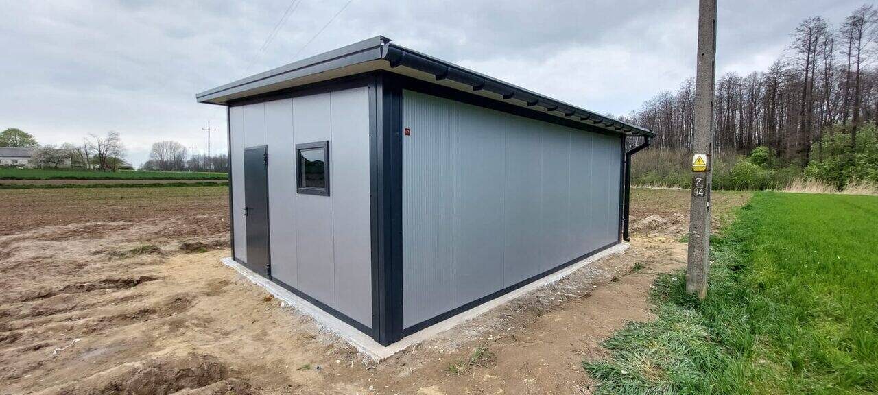 Grey insulated PIR garage with anthracite trim and a side window, front three-quarter view on a cleared plot