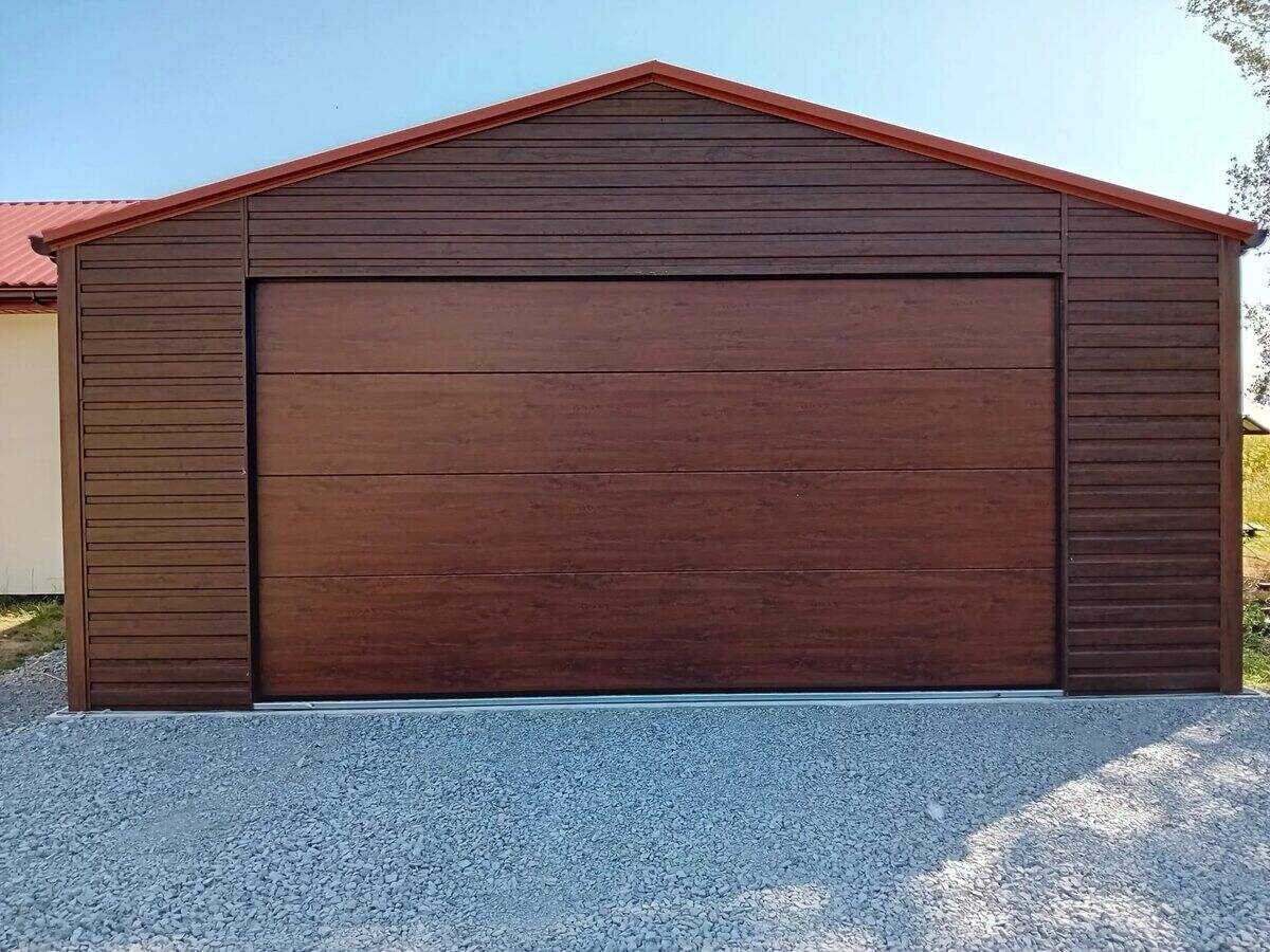 Steel garage with golden oak wood-effect finish, front three-quarter view in countryside setting