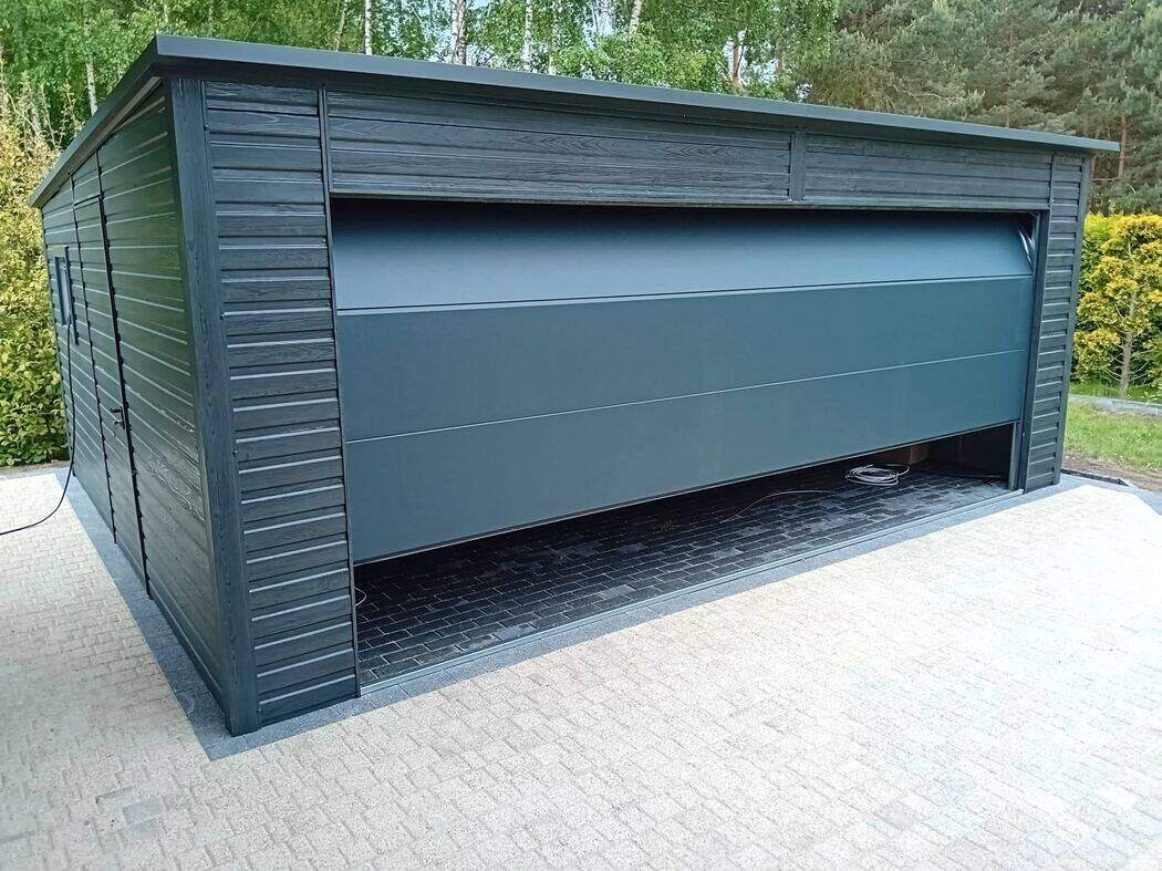 Anthracite steel garage, front three-quarter view beside an evergreen hedge