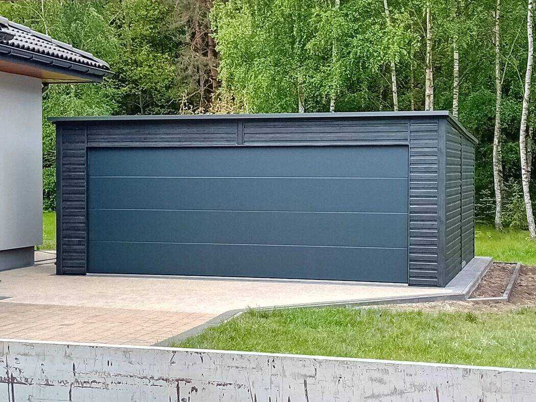 Anthracite steel garage with the sectional door partially raised, front view on concrete driveway