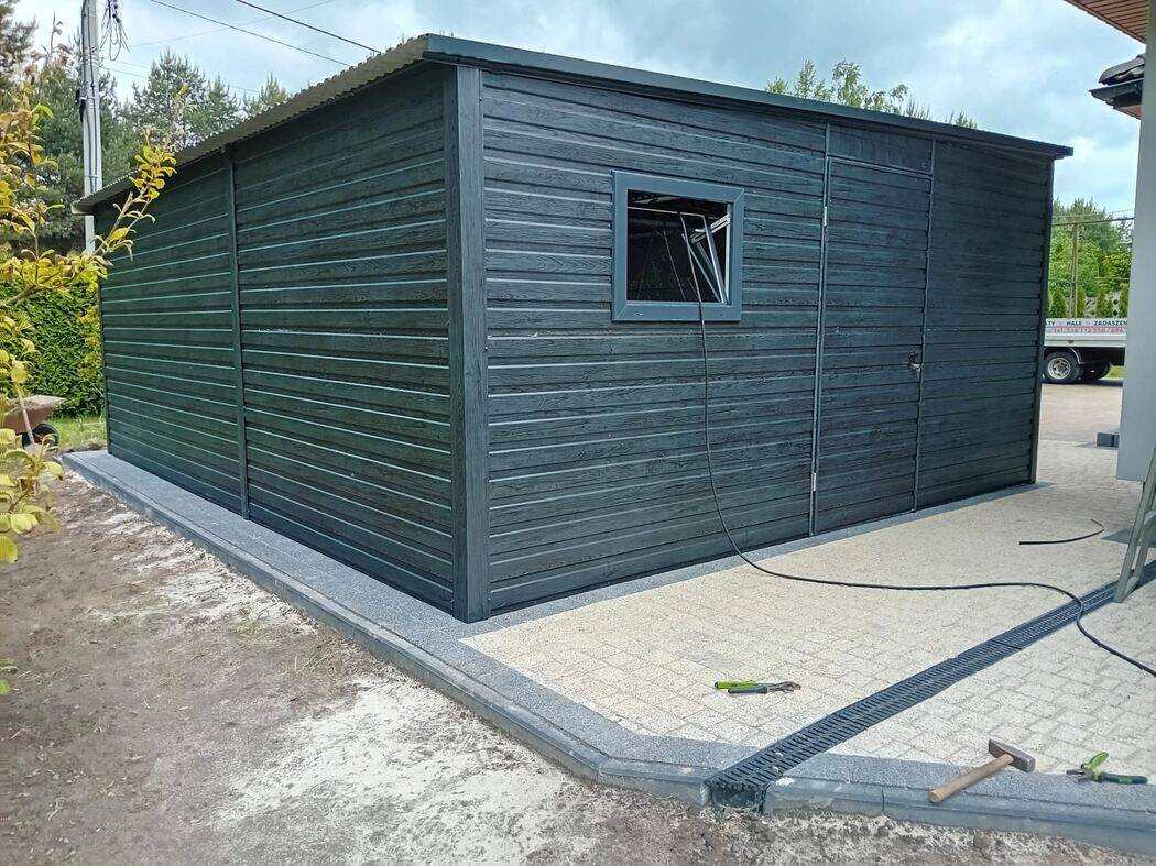 Anthracite steel garage with side door visible, front three-quarter view on concrete driveway