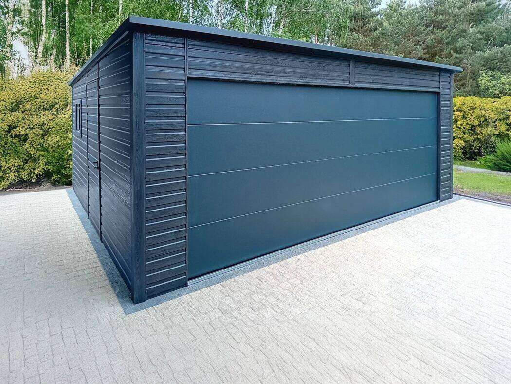 Anthracite steel garage, front three-quarter view on concrete driveway with pine trees in background