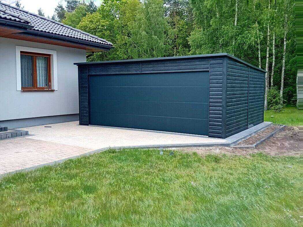 Anthracite steel garage installed beside a house, front-left three-quarter view with birch trees