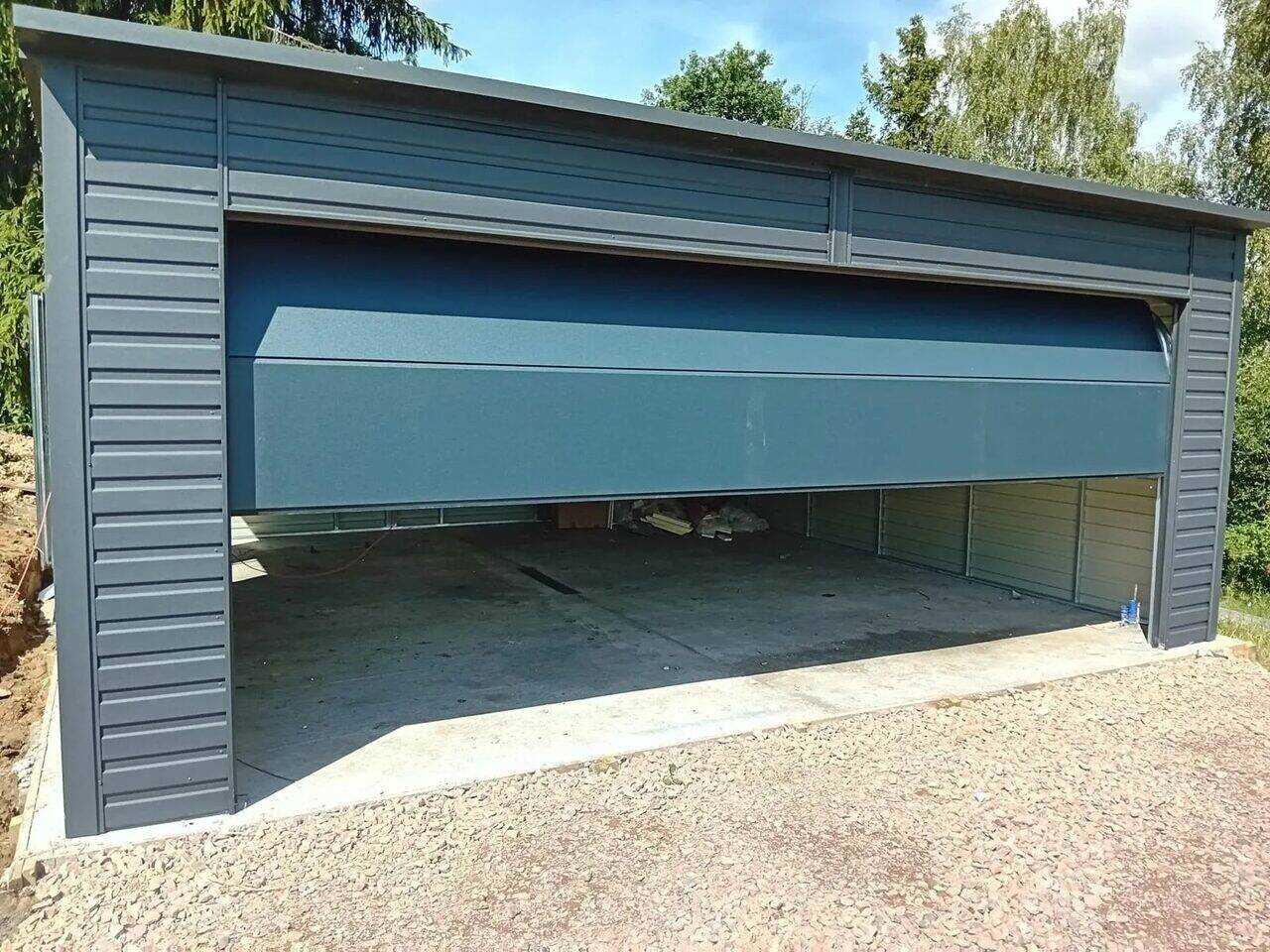 Anthracite steel garage with the sectional door fully open, front three-quarter view on gravel