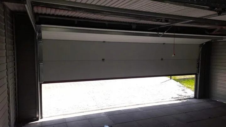 View from inside a steel garage looking out through the open sectional door onto the driveway
