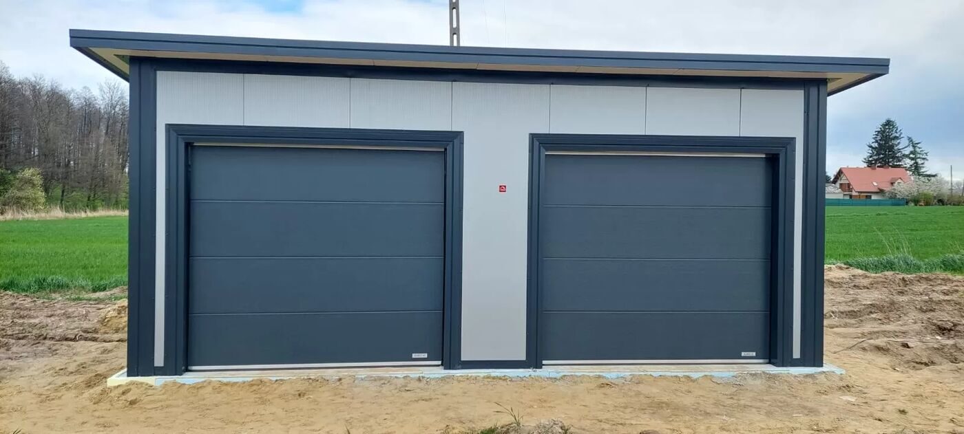 Insulated double garage with two anthracite sectional doors, front view on a cleared plot