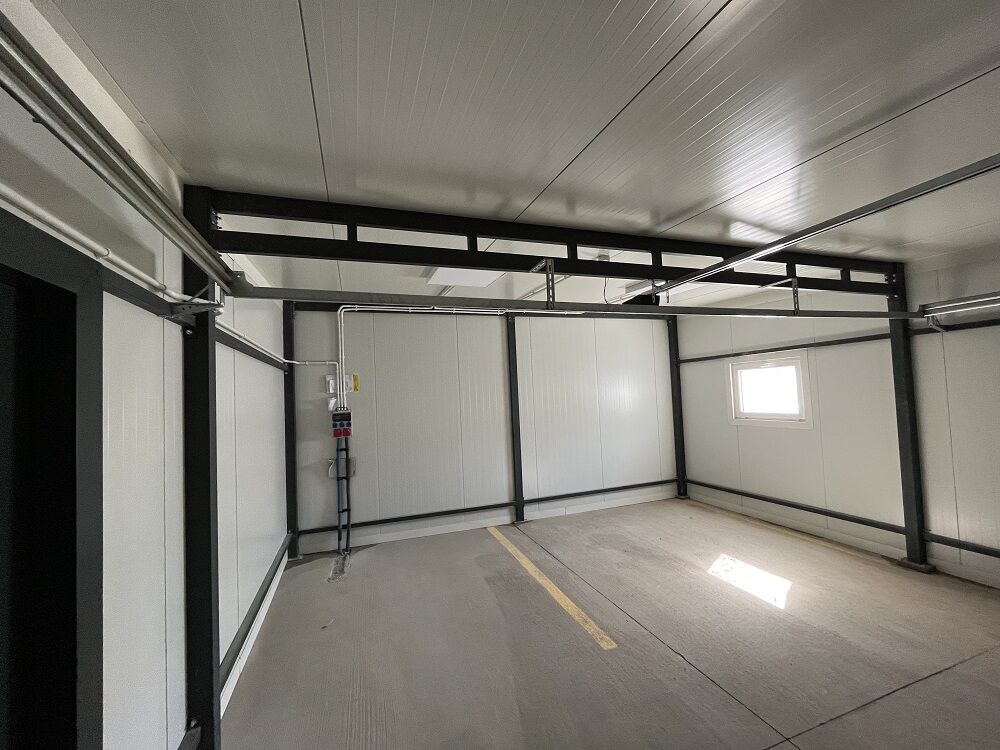 Inside an insulated garage: lit panel walls, a window and a dark steel frame