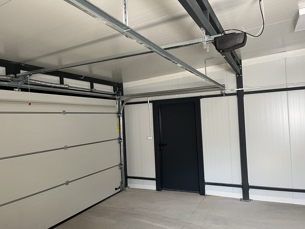 Close-up of an insulated garage's sectional door track and opener hardware, side door visible