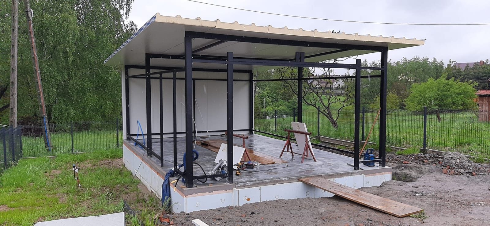Insulated garage steel frame with the roof panel and part of the wall cladding fitted, tools on the base