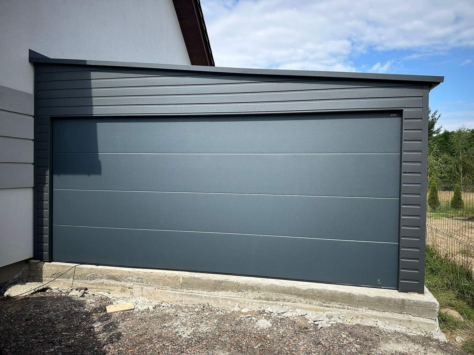 Grey steel garage with a rear-pitch roof, attached to a house, front elevation, door closed