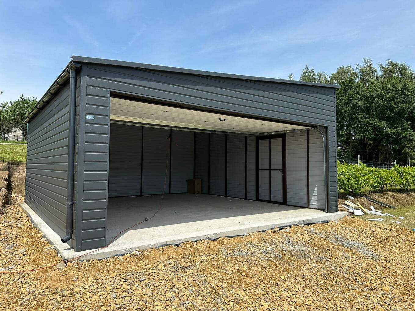 Interior of a dark grey steel garage with the door open onto a gravel yard