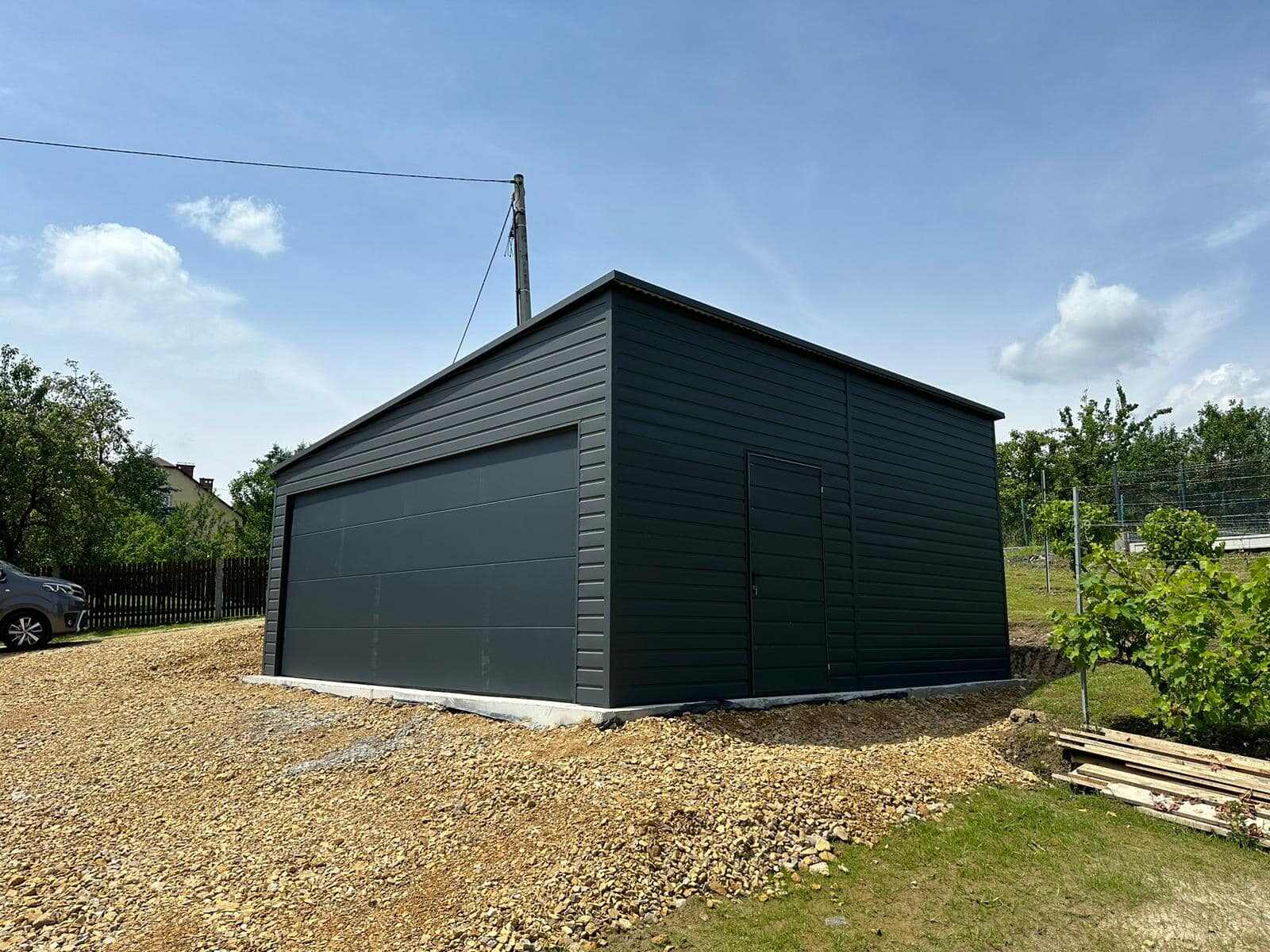 Dark anthracite steel garage, gable-end three-quarter view beside a clipped hedge