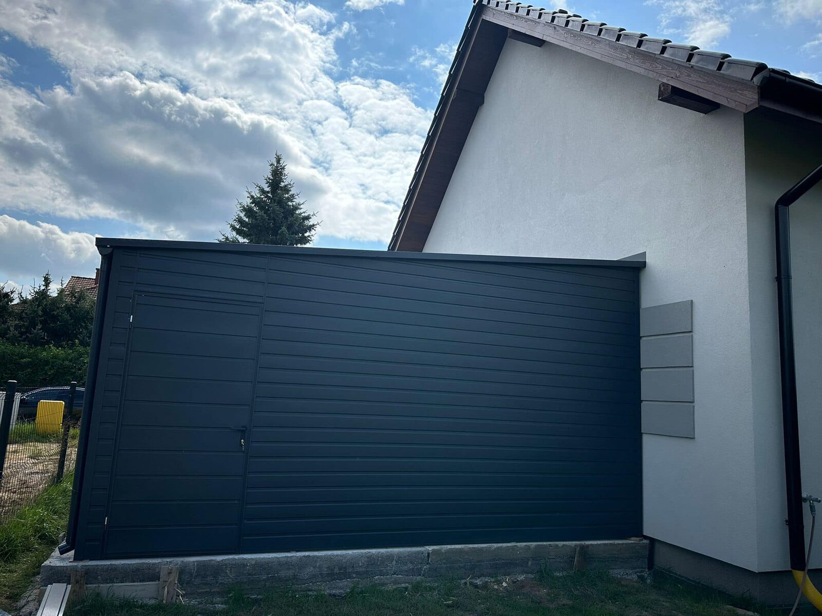 Dark grey steel garage with a side entrance door, attached to a white house, side elevation