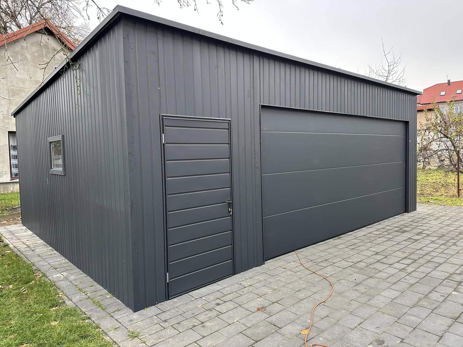 Anthracite steel garage with vertical cladding, one wide sectional door, a side entrance door and a small window