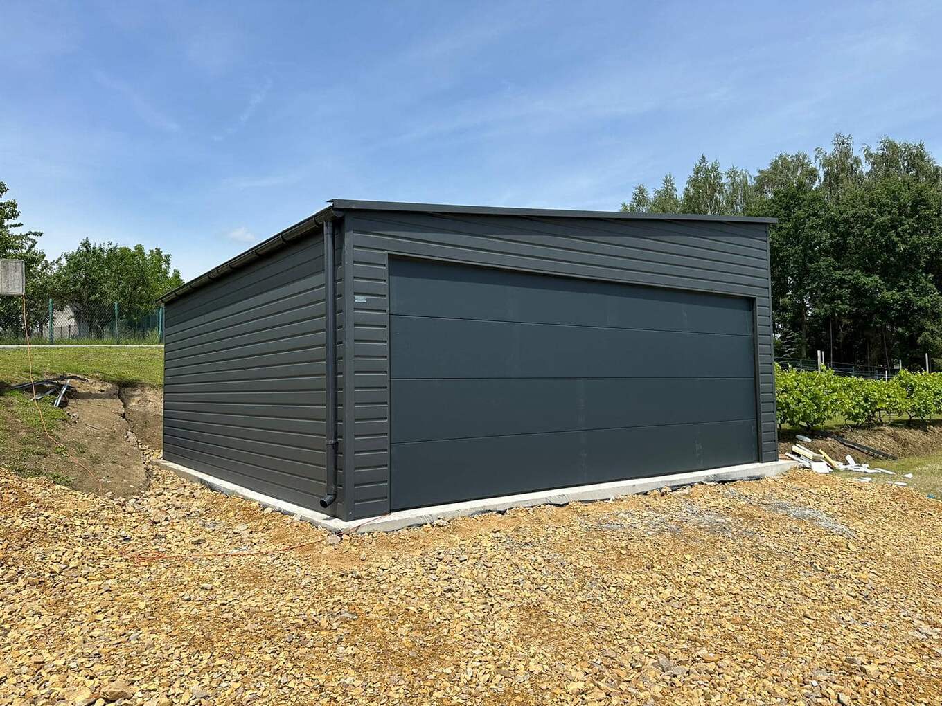 Dark anthracite steel garage, gable-end three-quarter view on a gravel base