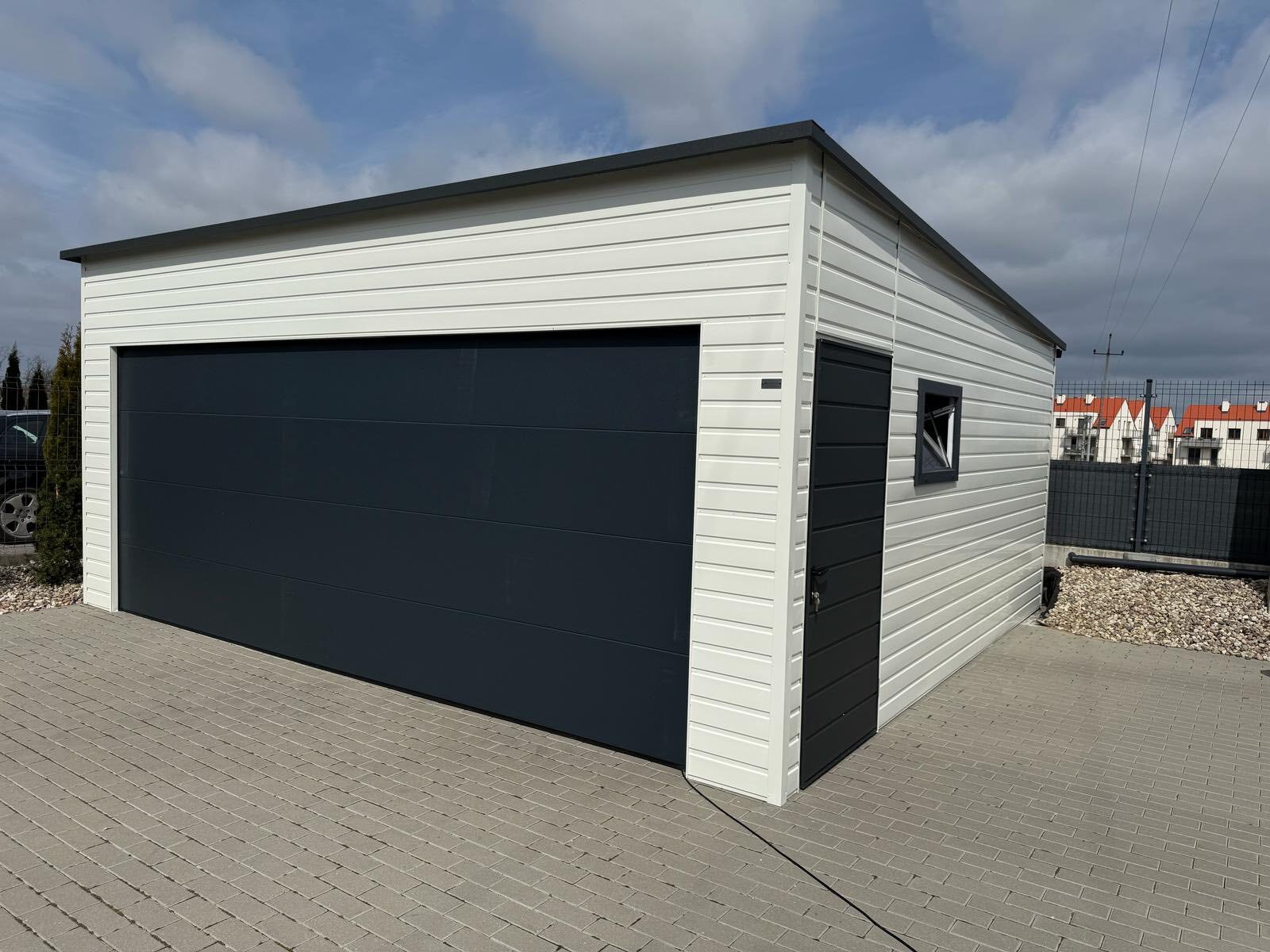 White-clad steel garage with one wide anthracite sectional door, a side entrance door and a small window