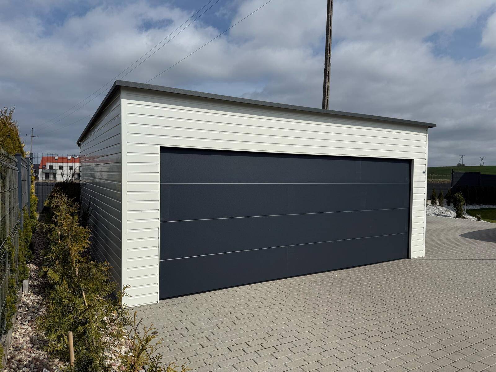 White-clad steel garage with one wide anthracite sectional door, seen at an angle