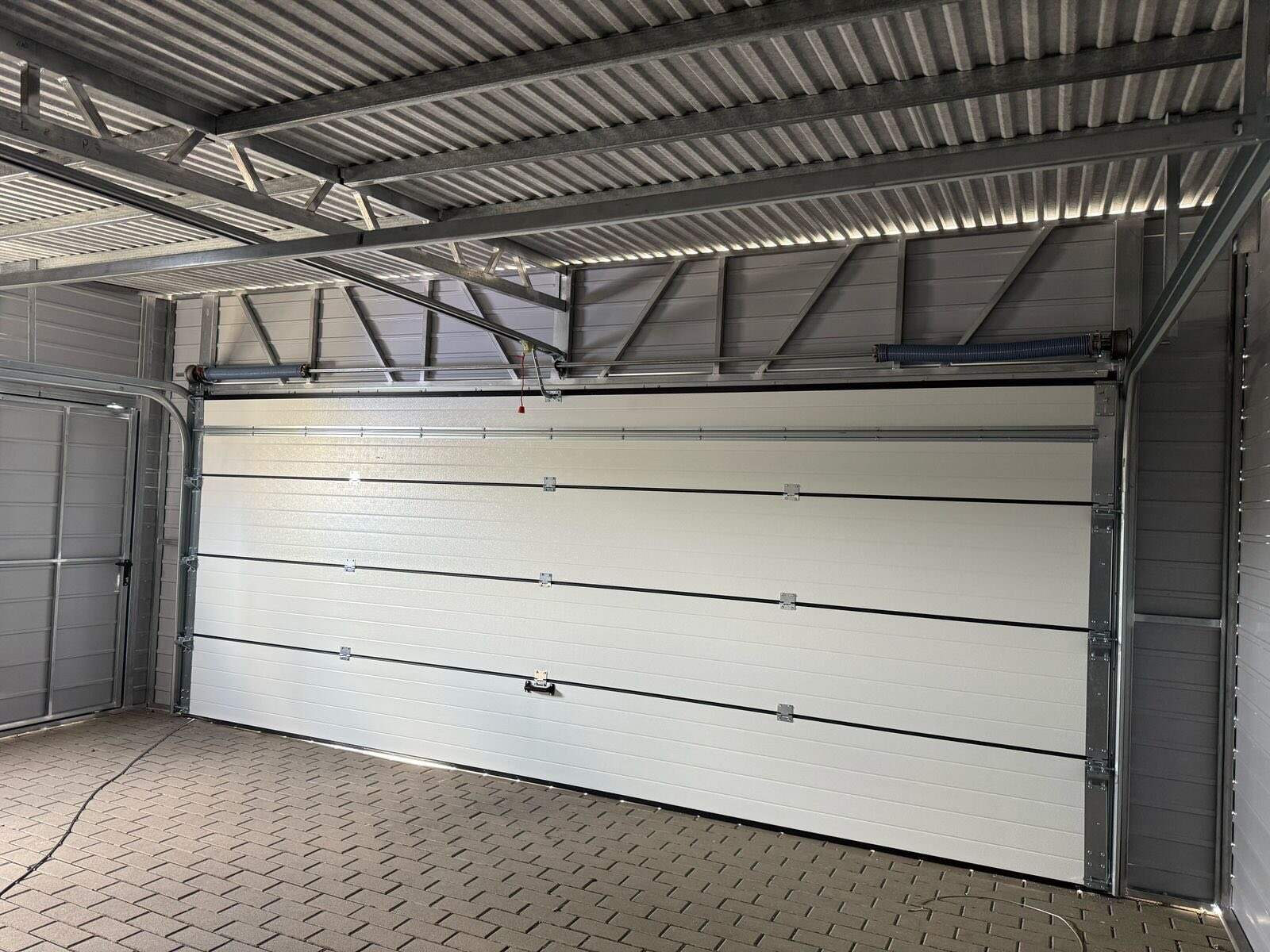 Inside a steel garage: a white sectional door on its automatic opener, the side entrance door and the galvanised roof frame