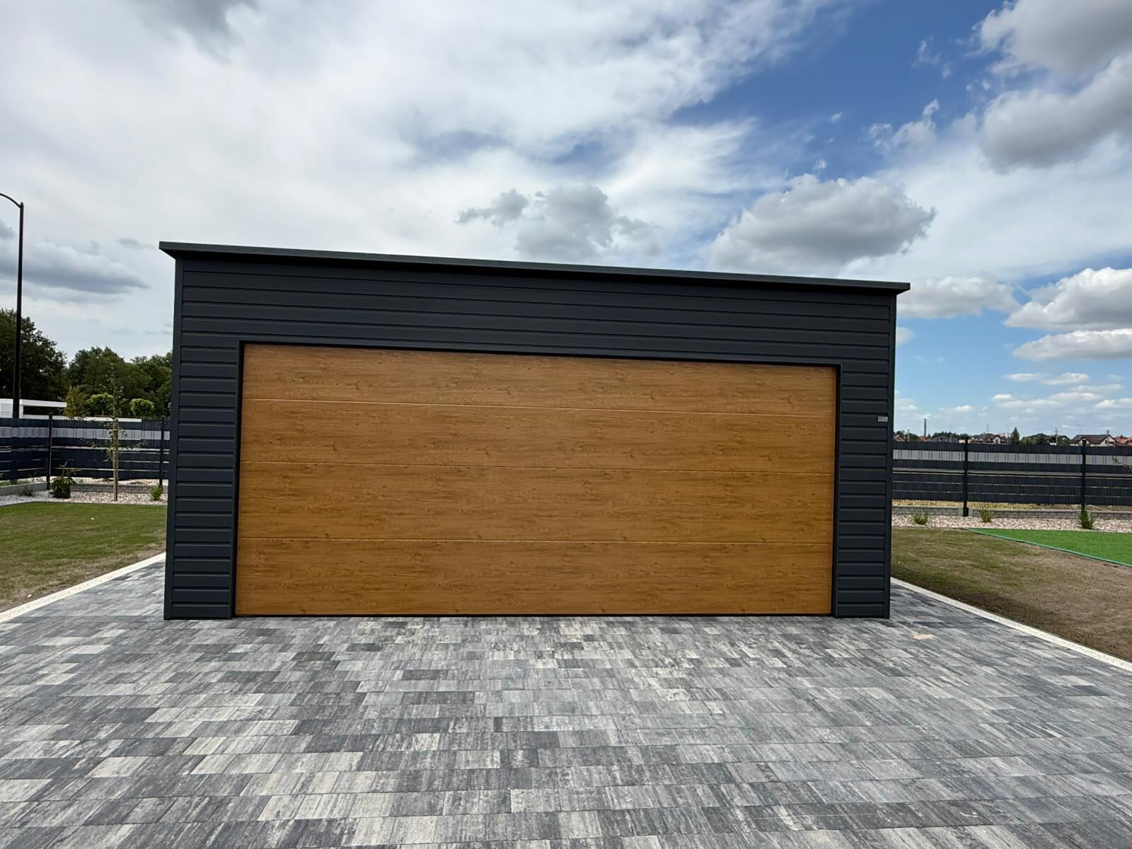 Dark steel garage with a wood-effect sectional door and a rear-pitch roof, front elevation
