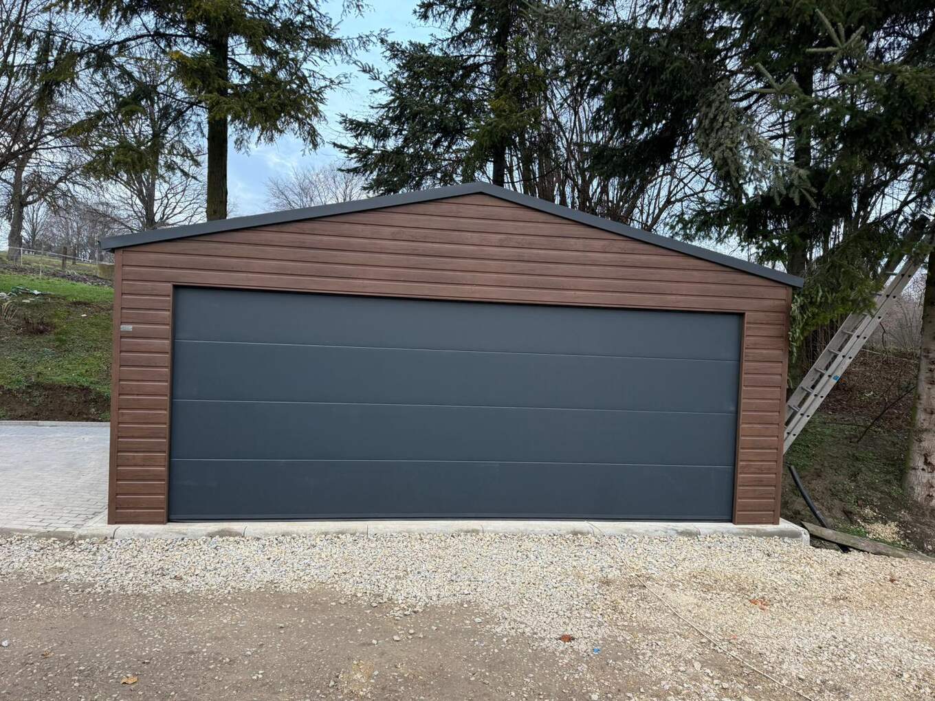 Brown wood-effect steel garage with an apex roof and one wide anthracite sectional door