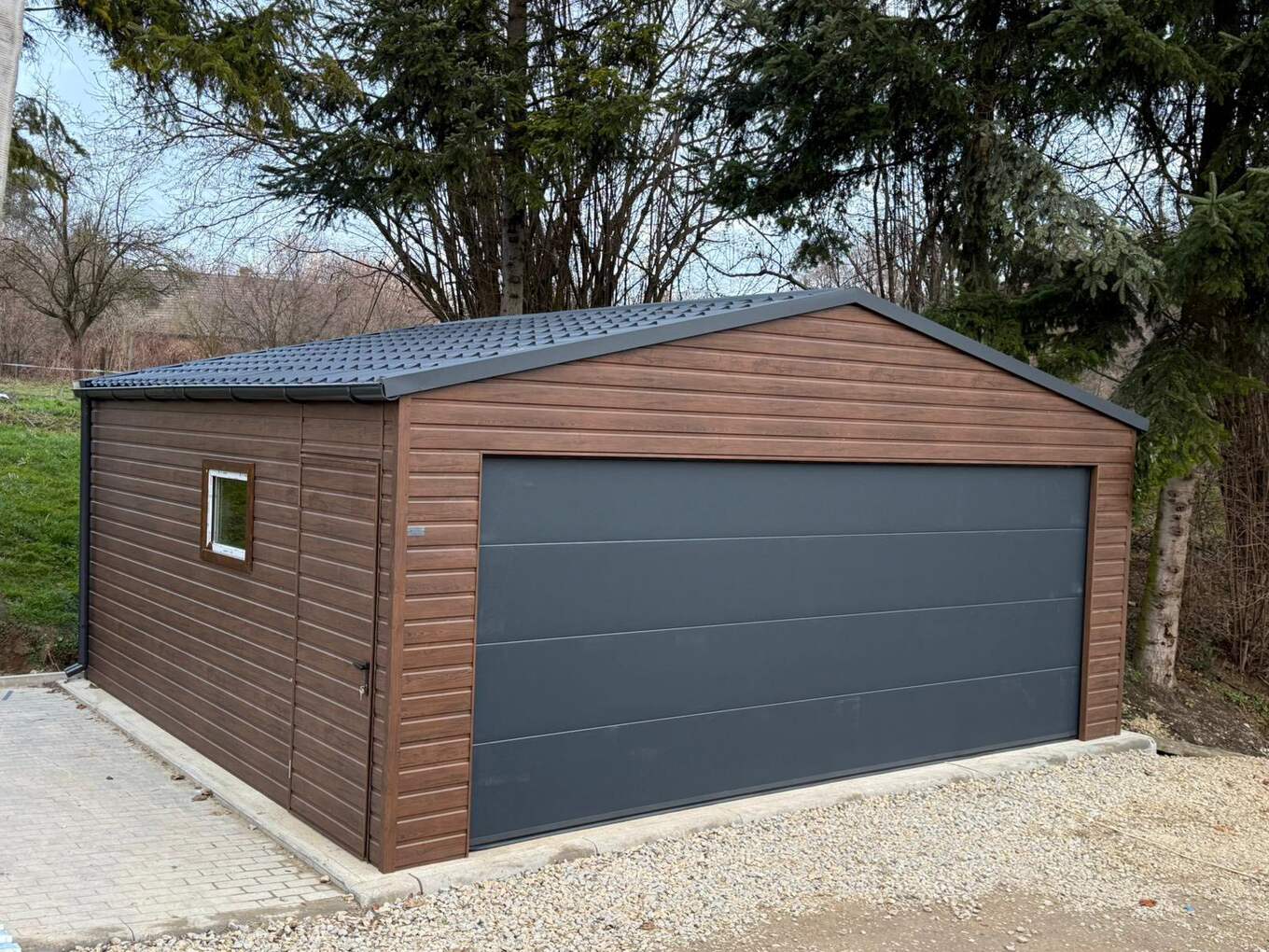 Wood-effect steel garage with an apex roof, one wide grey sectional door, and a side window and entrance door
