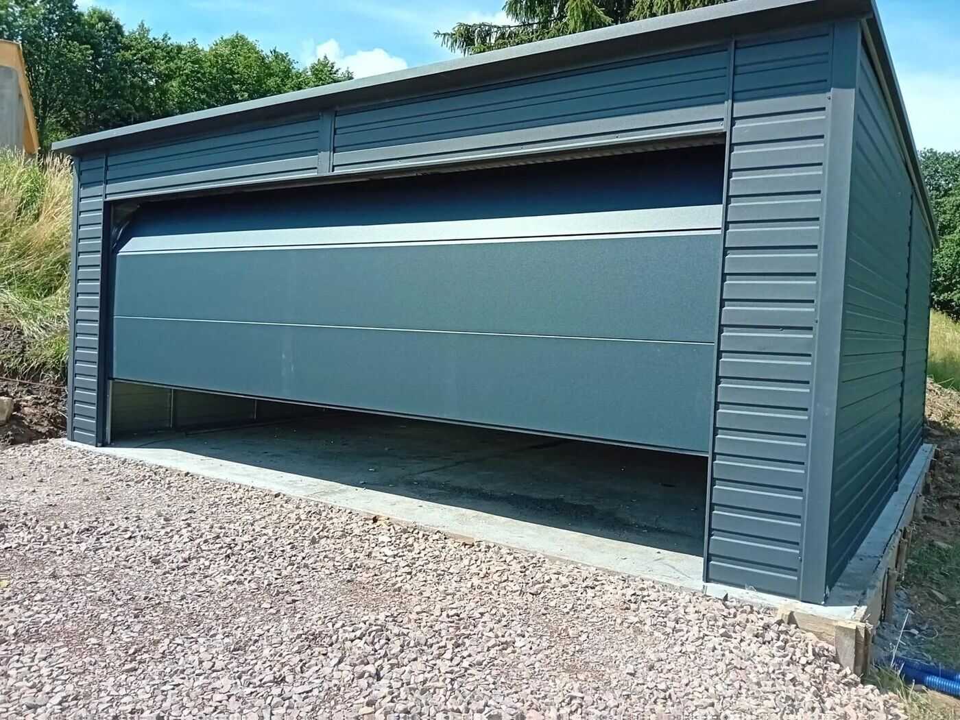 Anthracite steel single garage with the door open, front view on gravel